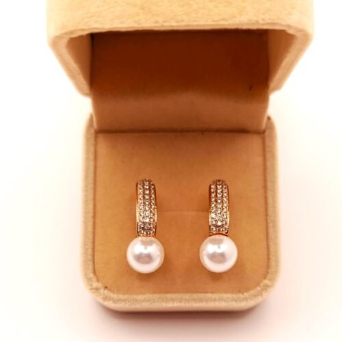 Επιχρυσωμένα Τα Xuping skoularikia SKU1G05 είναι χρυσά σκουλαρίκια με λευκά μαργαριτάρια και μικρούς πολύτιμους λίθους, που παρουσιάζονται σε ανοιχτό μπεζ βελούδινο κουτί κοσμημάτων.