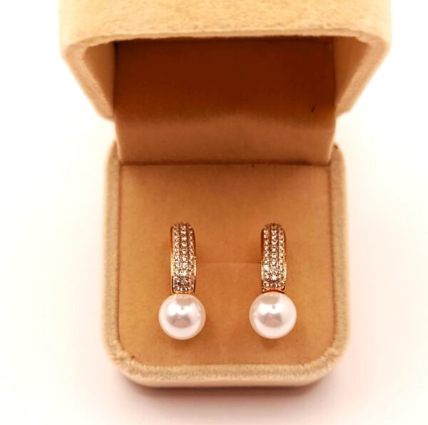 Επιχρυσωμένα Τα Xuping skoularikia SKU1G05 είναι χρυσά σκουλαρίκια με λευκά μαργαριτάρια και μικρούς πολύτιμους λίθους, που παρουσιάζονται σε ανοιχτό μπεζ βελούδινο κουτί κοσμημάτων.