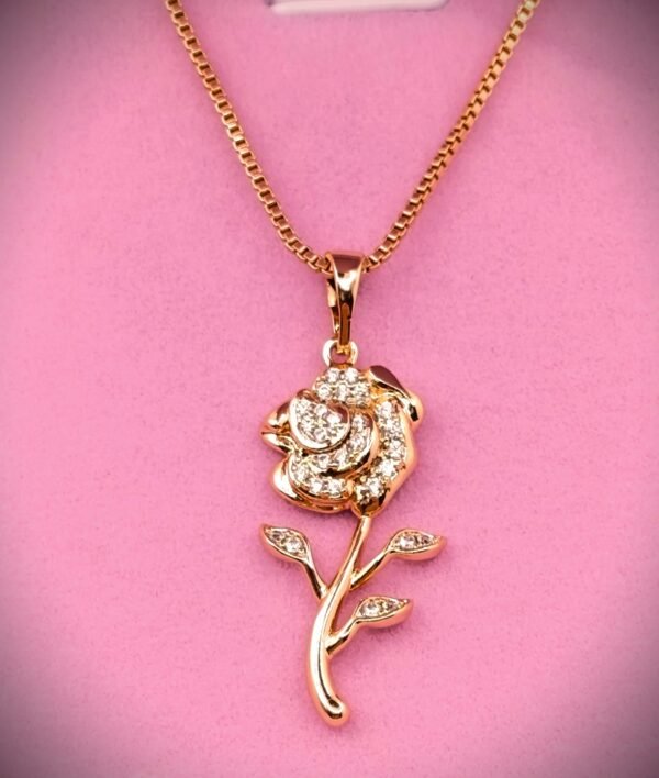 Επιχρυσωμένα Το Xuping Επιχρυσωμένo Κολιέ SKU 2G01 διαθέτει ένα χρυσό κρεμαστό κόσμημα σε σχήμα τριαντάφυλλου, διακοσμημένο με λαμπερά διαμάντια στα πέταλα, τα φύλλα και το στέλεχος, που εμφανίζονται όμορφα σε ροζ φόντο.