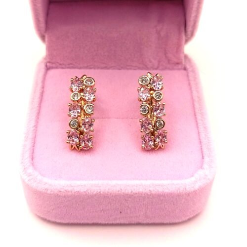 Επιχρυσωμένα Τα χρυσά σκουλαρίκια xuping-skoularikia-model-6, διακοσμημένα με ροζ και διάφανους πολύτιμους λίθους, παρουσιάζονται όρθια σε ανοιχτό ανοιχτό ροζ βελούδινο κουτί κοσμημάτων.