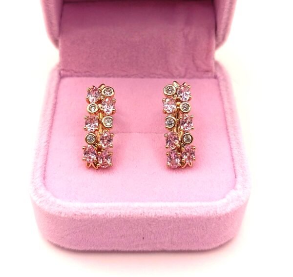 Επιχρυσωμένα Τα χρυσά σκουλαρίκια xuping-skoularikia-model-6, διακοσμημένα με ροζ και διάφανους πολύτιμους λίθους, παρουσιάζονται όρθια σε ανοιχτό ανοιχτό ροζ βελούδινο κουτί κοσμημάτων.